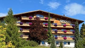 Un hotel de varios pisos con balcones, rodeado de vegetación y árboles.