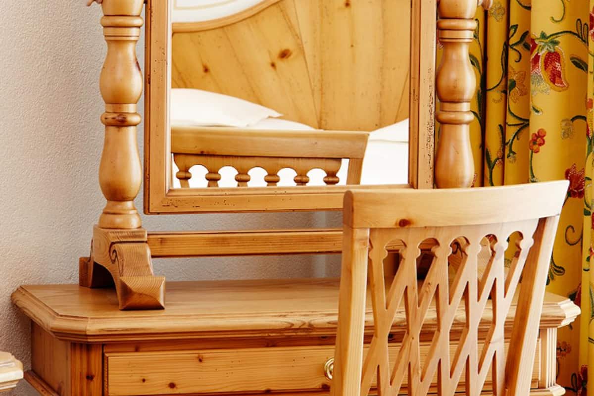 Ein Holztisch mit Spiegel, ein Stuhl und ein Bett mit hölzernem Kopfteil.