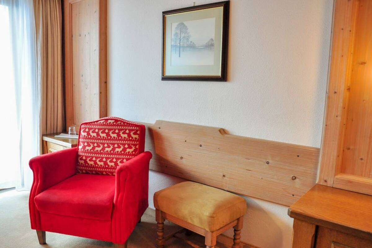 Ein Zimmer mit einer hölzernen Sitzbank, einem roten Sessel mit gemustertem Kissen und einem gerahmten Bild an der Wand.