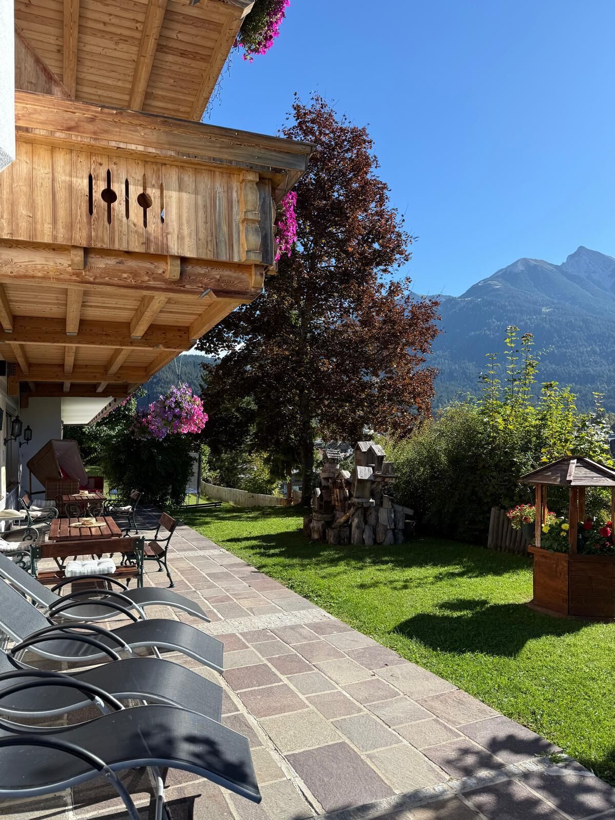 Ein Holzgebäude mit überdachter Terrasse, Sitzmöglichkeiten im Freien und Blick auf Berge.
