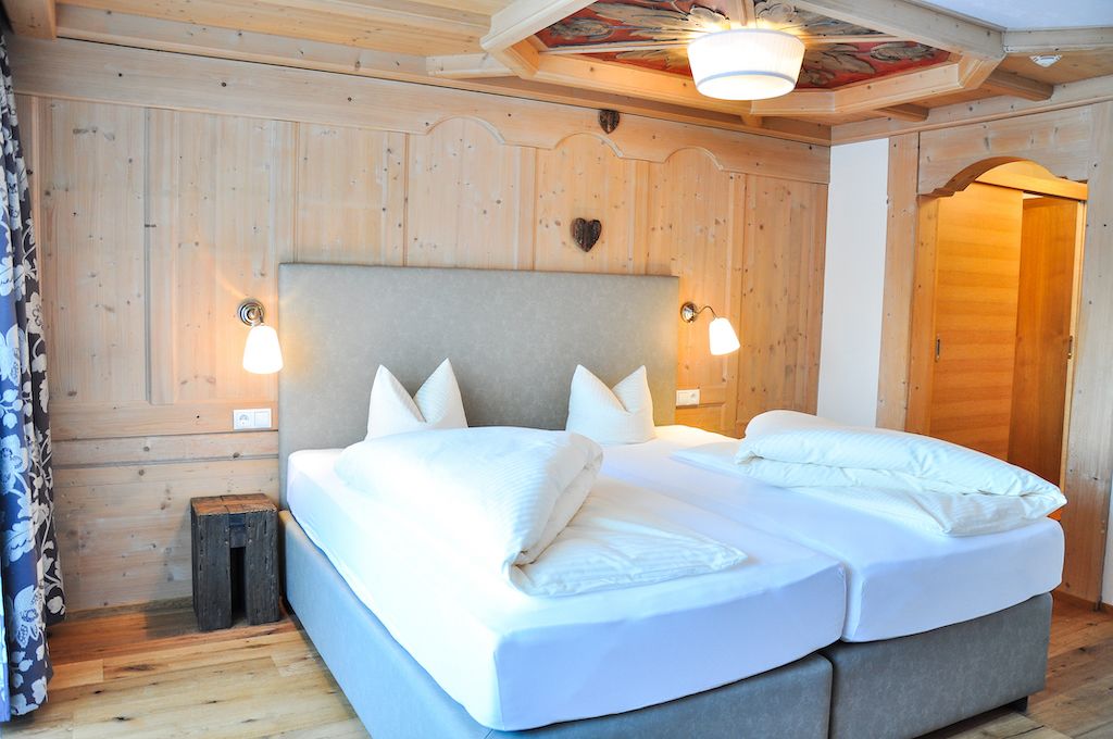 Cama doble con sábanas blancas en una habitación de madera con dos lámparas fijadas a la pared.