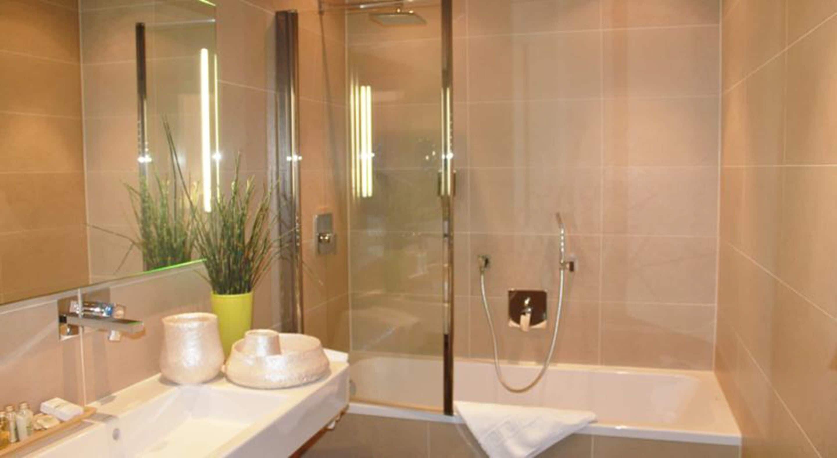 Un baño moderno con cabina de ducha de vidrio, un lavabo blanco y una planta en maceta.