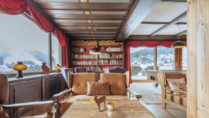 A cozy reading room with leather chairs, a wooden coffee table, and a bookshelf filled with books. - Seelos (Seefeld in Tirol)