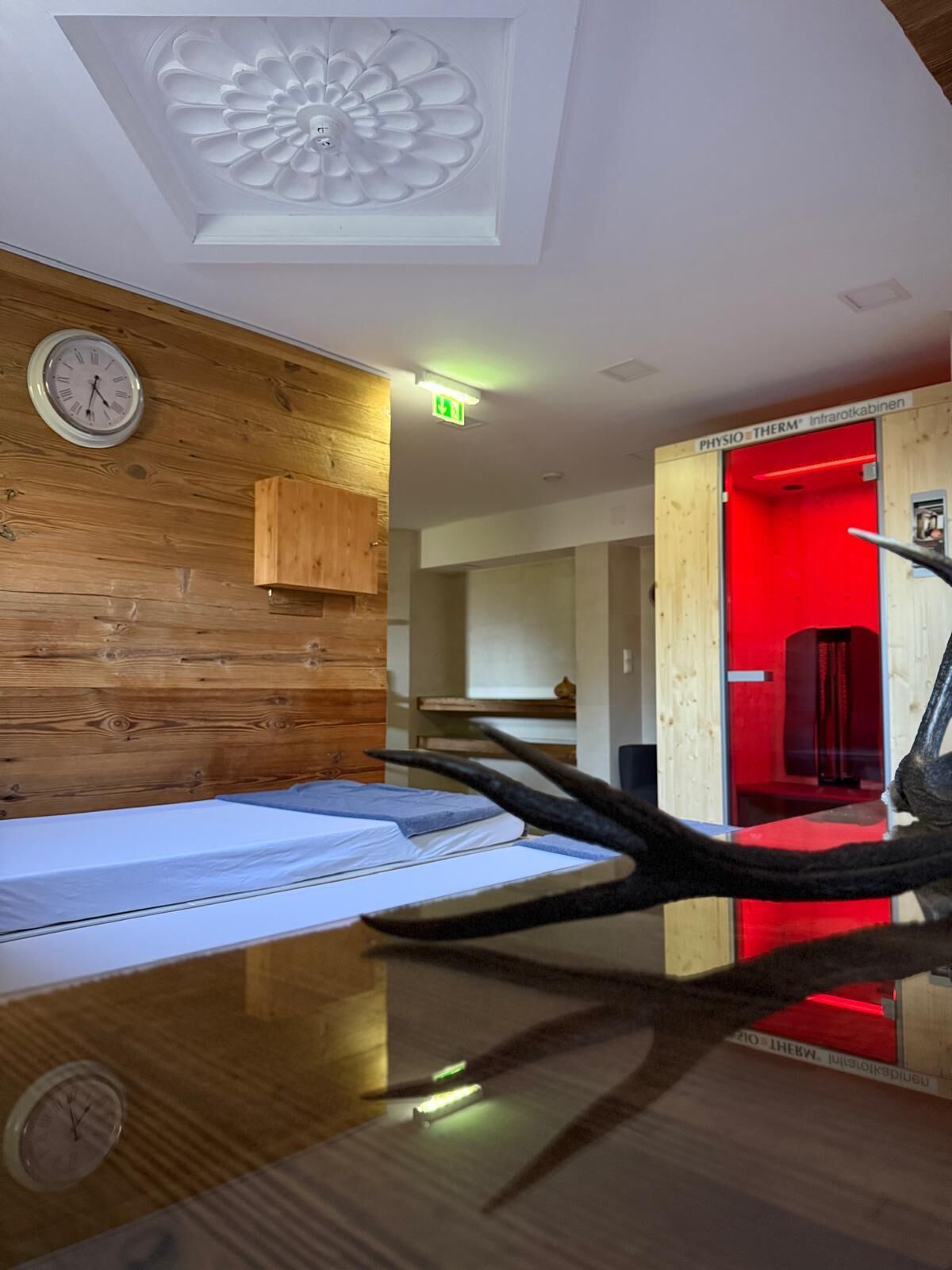 Habitación de hotel con paneles de madera, una cama, un reloj y un mueble con iluminación roja.