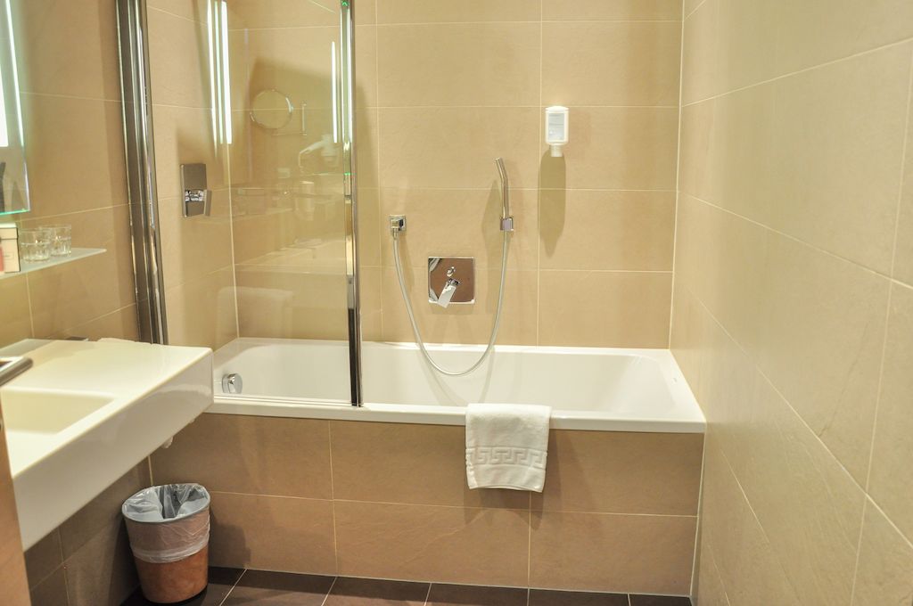 A modern bathroom with a bathtub, a glass shower enclosure, a sink, and a trash bin.