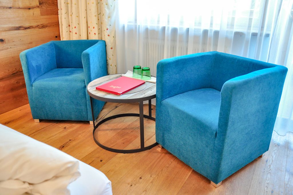 A room with two blue armchairs, a small round table with a red book, and a window with curtains.