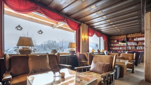 A cozy room with a wooden ceiling, leather sofas, a glass coffee table, and a bookshelf filled with books. - Seelos (Seefeld in Tirol)