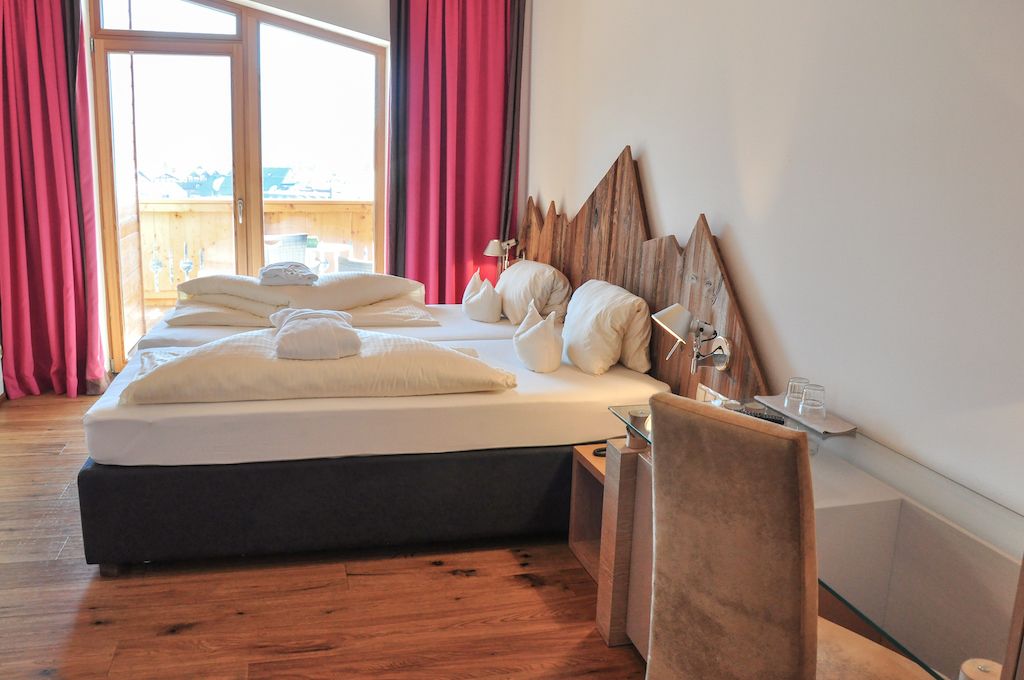 Hotelkamer met een groot bed, een houten hoofdbord, nachtkastje en uitzicht door een raam met gordijnen.