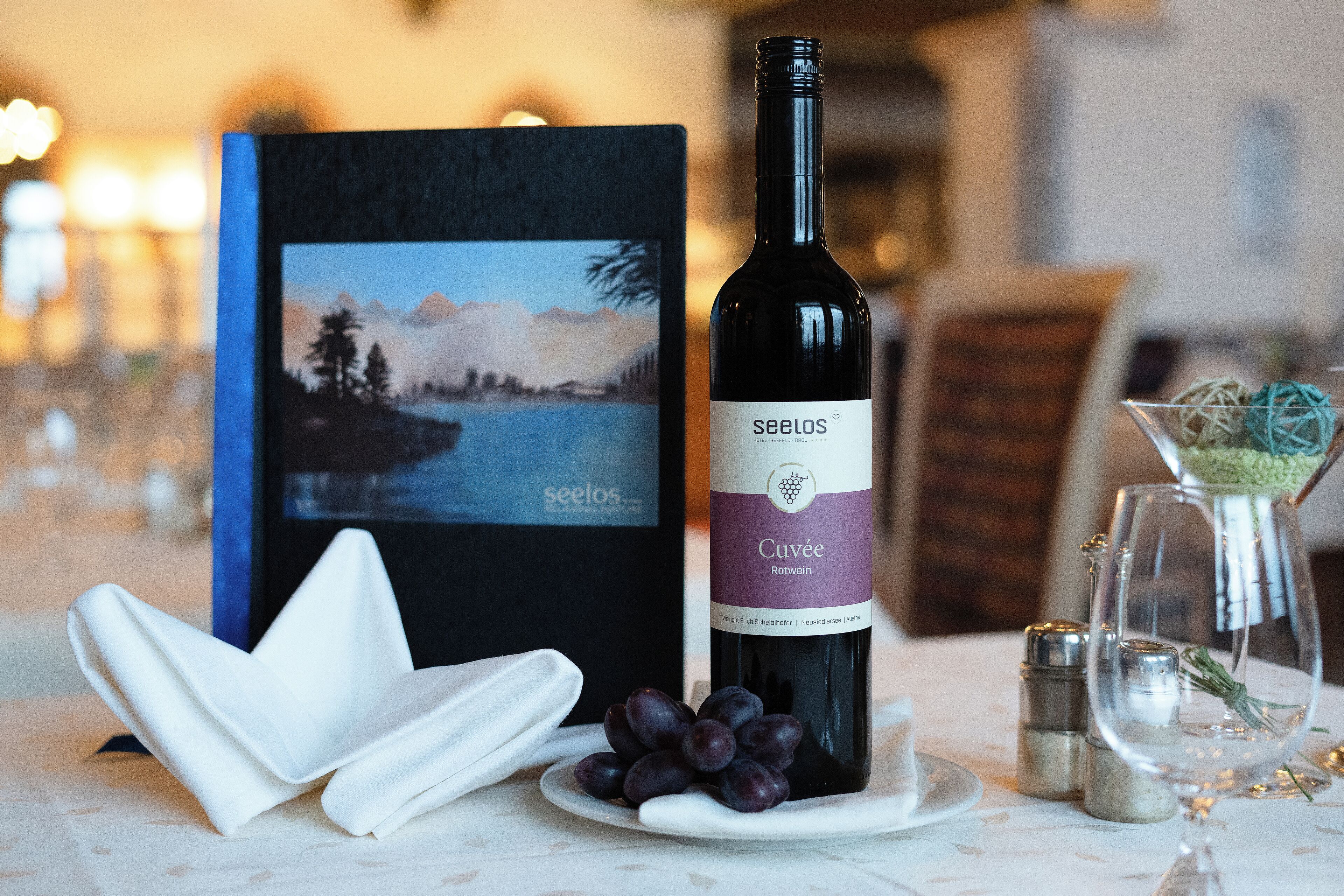A bottle of Seelos wine, a plate with grapes, and a decorative item on a table.