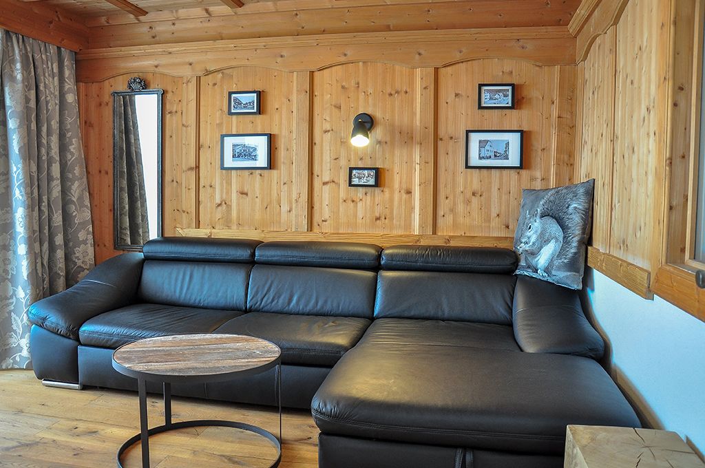 A wooden-paneled room with a black leather sofa, a round coffee table, and framed pictures on the walls.