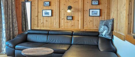 A wooden-paneled room with a black leather sofa, a round coffee table, and framed pictures on the walls.