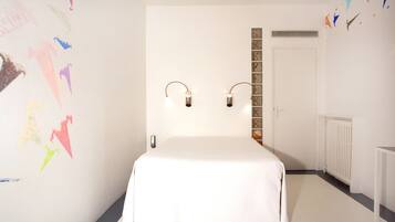 A bedroom with a bed, two wall-mounted lights, a radiator, and a door.