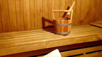 Un banc en bois pour sauna, avec une serviette et un seau en bois muni d’un manche en bois.