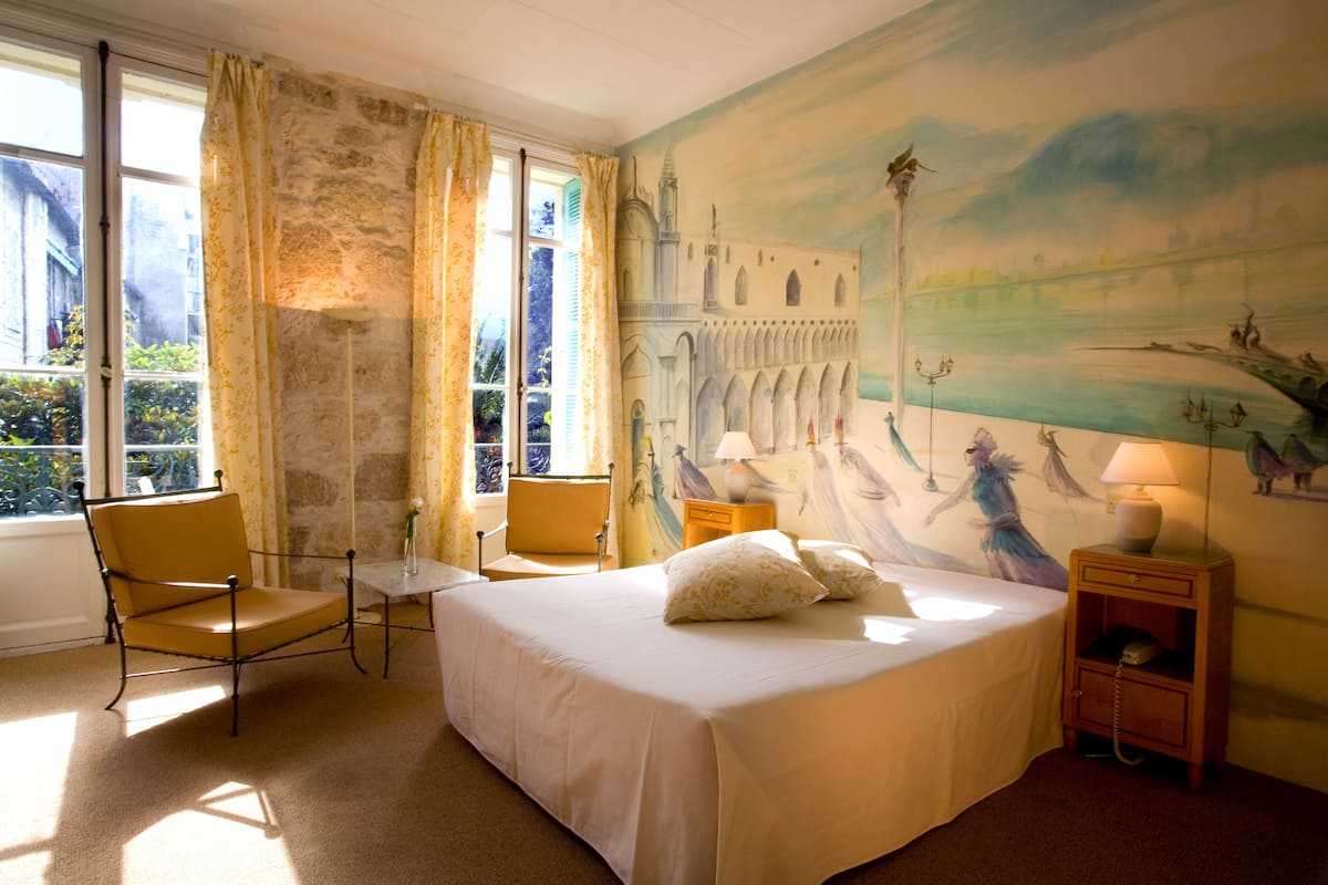 A hotel room with a bed, a chair, a table, and a nightstand.