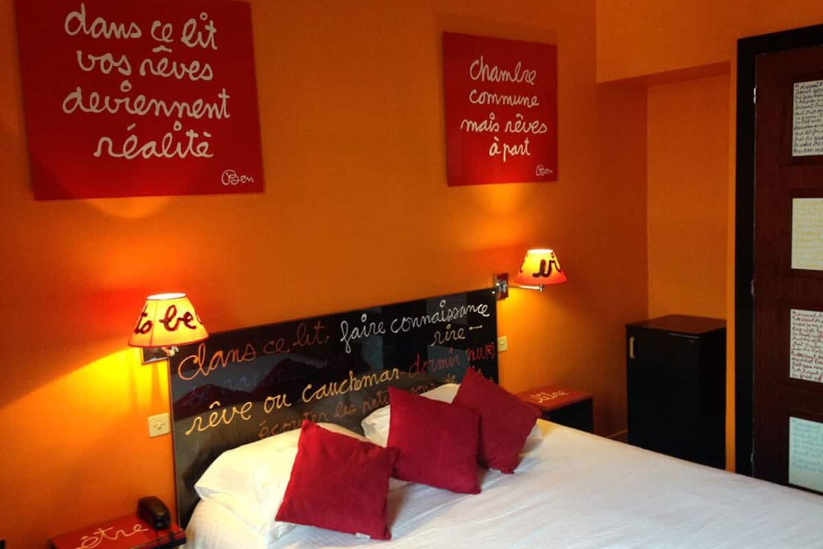 A hotel room with a bed, red pillows, two wall-mounted lamps, and motivational quotes on the walls.