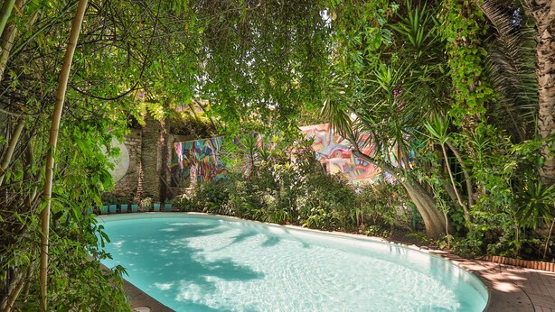 A swimming pool surrounded by lush greenery and a stone wall with colorful artwork. - Windsor Hotel (Nice)