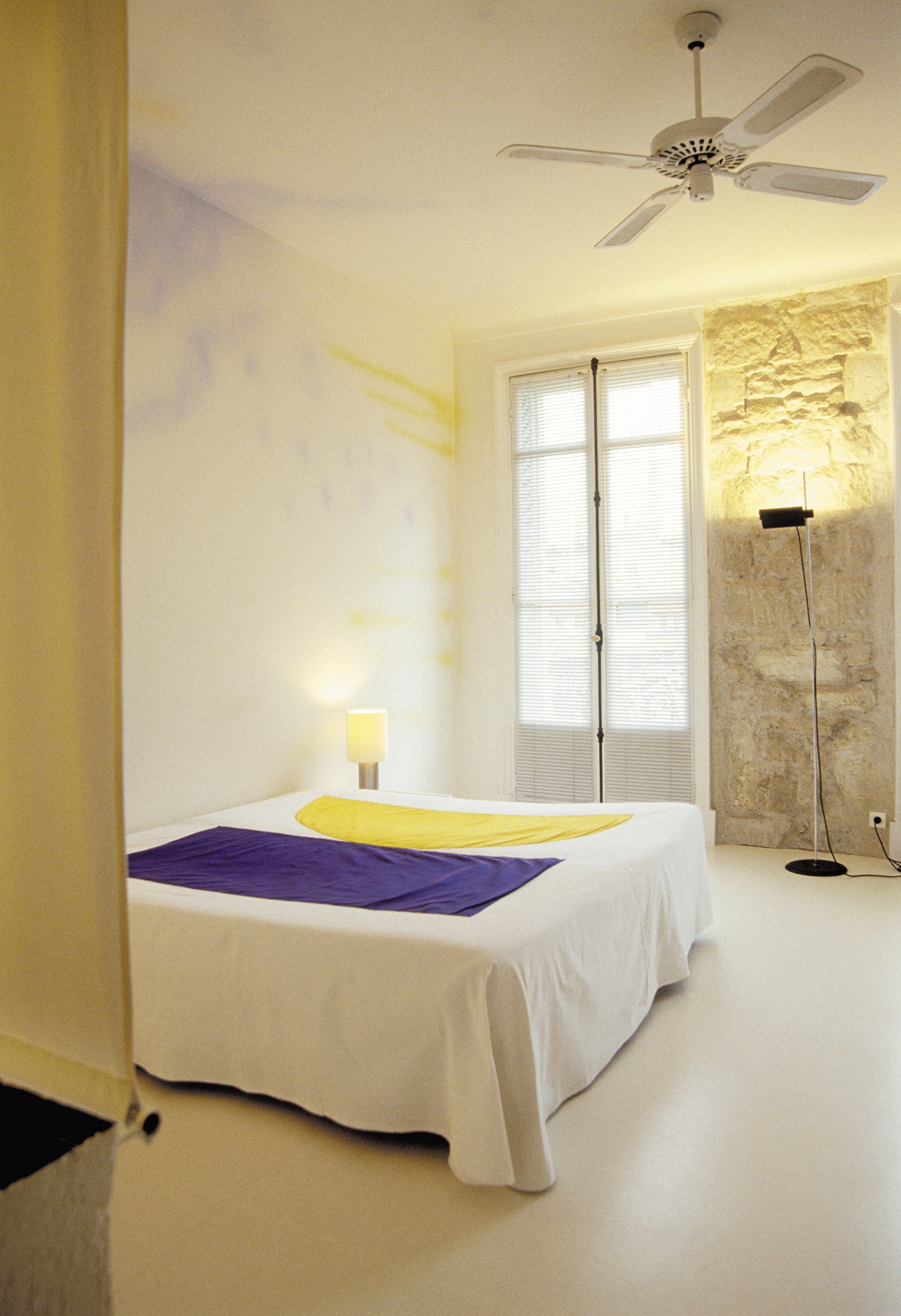 Un dormitorio con cama, ventilador de techo, lámpara de pie y pared de piedra.