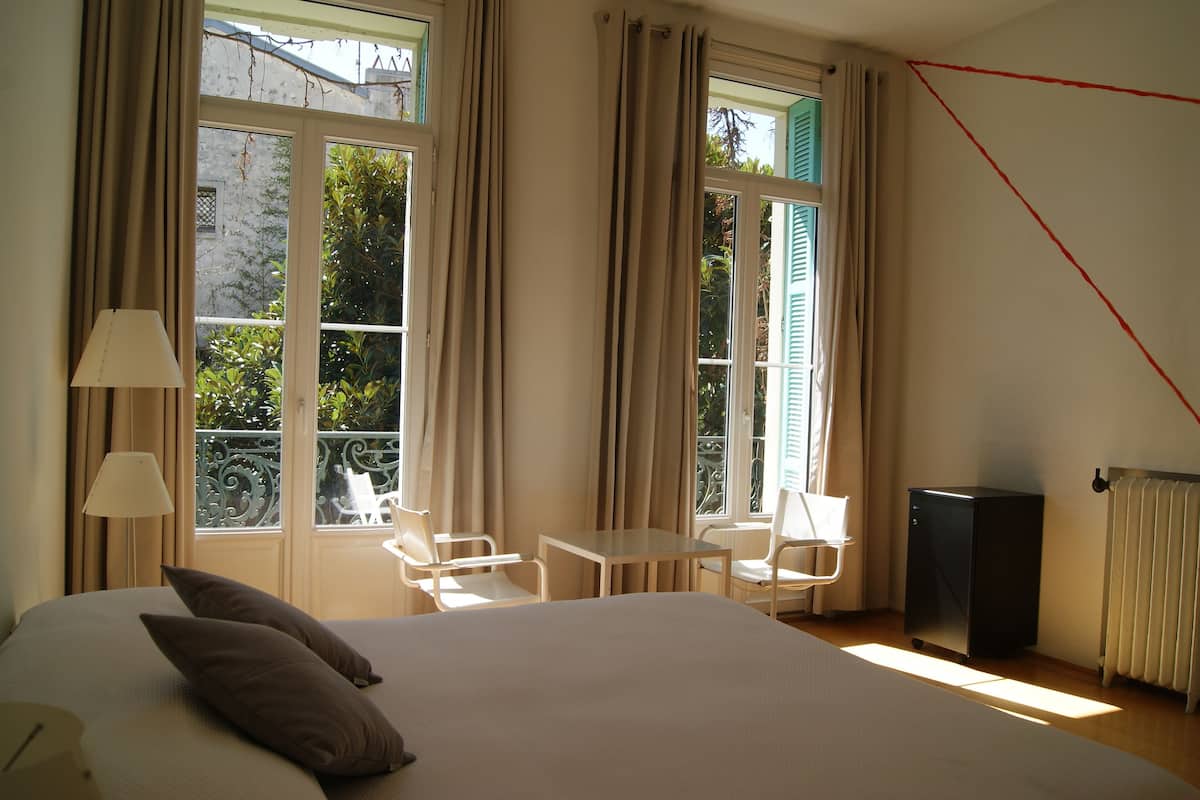 A hotel room with a bed, two chairs, a small table, and a radiator.