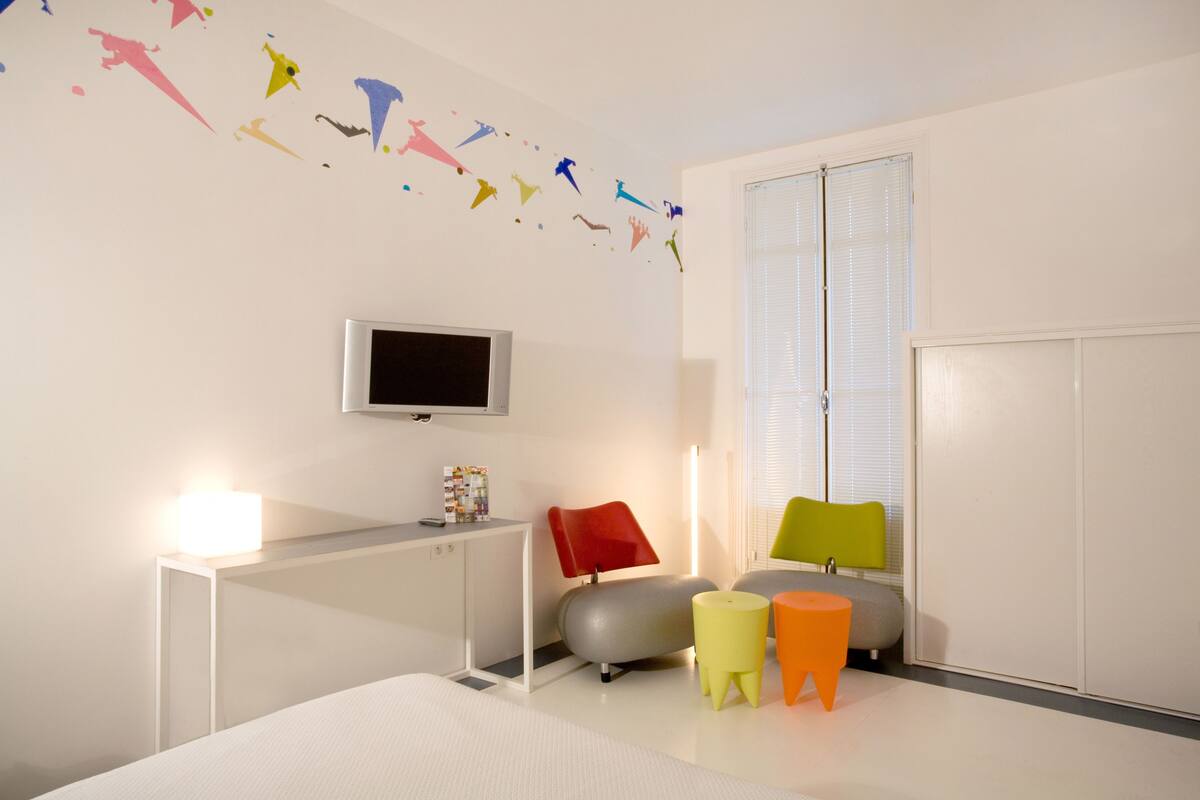 A modern bedroom with a bed, a desk, a TV, and colorful wall decorations.