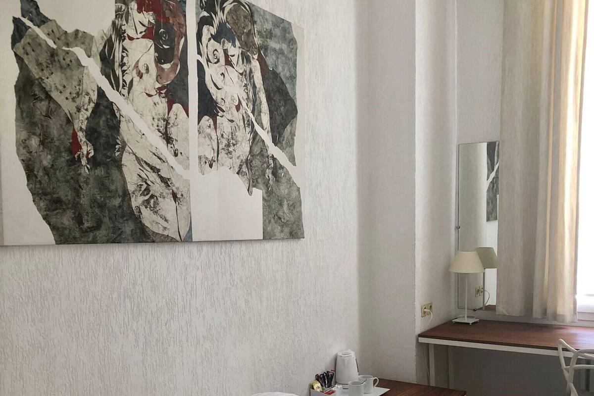 A hotel room with a bed, a desk, and two paintings on the wall.