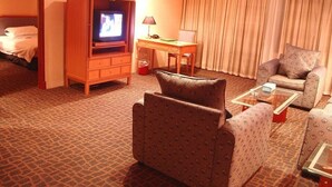 A hotel room with a television, a desk with a lamp, two patterned armchairs, a glass coffee table, and a bed with a headboard. - Shanghai Changhang Hotel (Shanghai)
