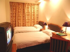 Ein Hotelzimmer mit zwei Betten, einem Fernseher, einem Schreibtisch mit Telefon und einer Lampe.
