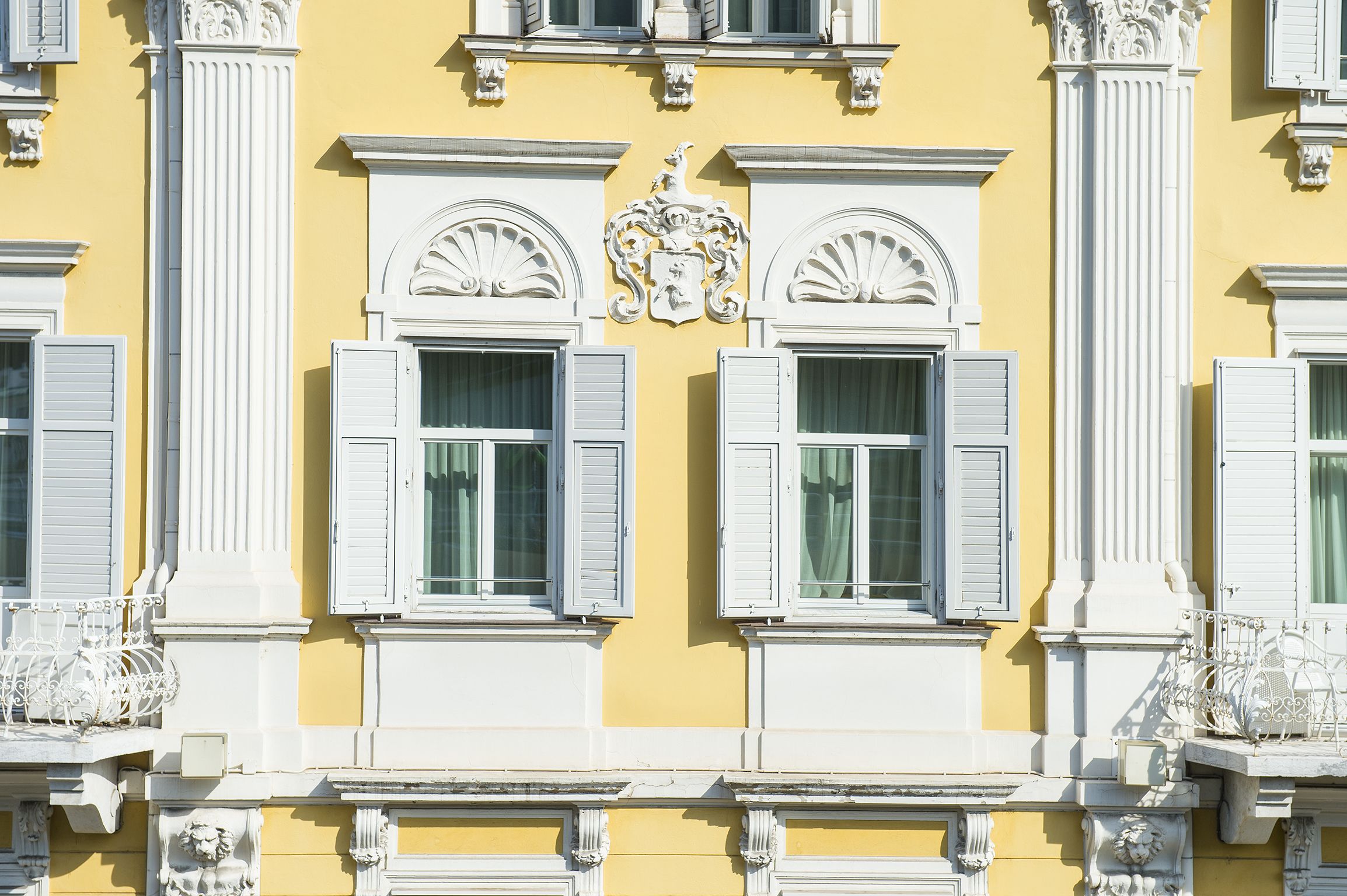 A building facade with symmetrical windows, white shutters, and ornate architectural details.