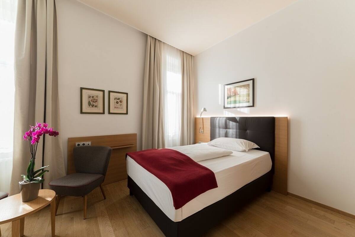 A hotel room with a bed, a chair, a table, and a potted plant.
