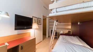 Een compacte hotelkamer met een stapelbed, een bureau met lamp, een flatscreen televisie en ingekaderde foto's aan de muur.