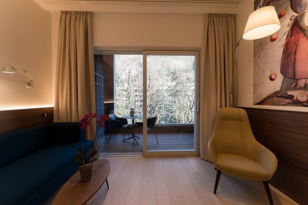 A modern living room with a blue sofa, a yellow armchair, a wooden coffee table, and a large window with a view of trees.