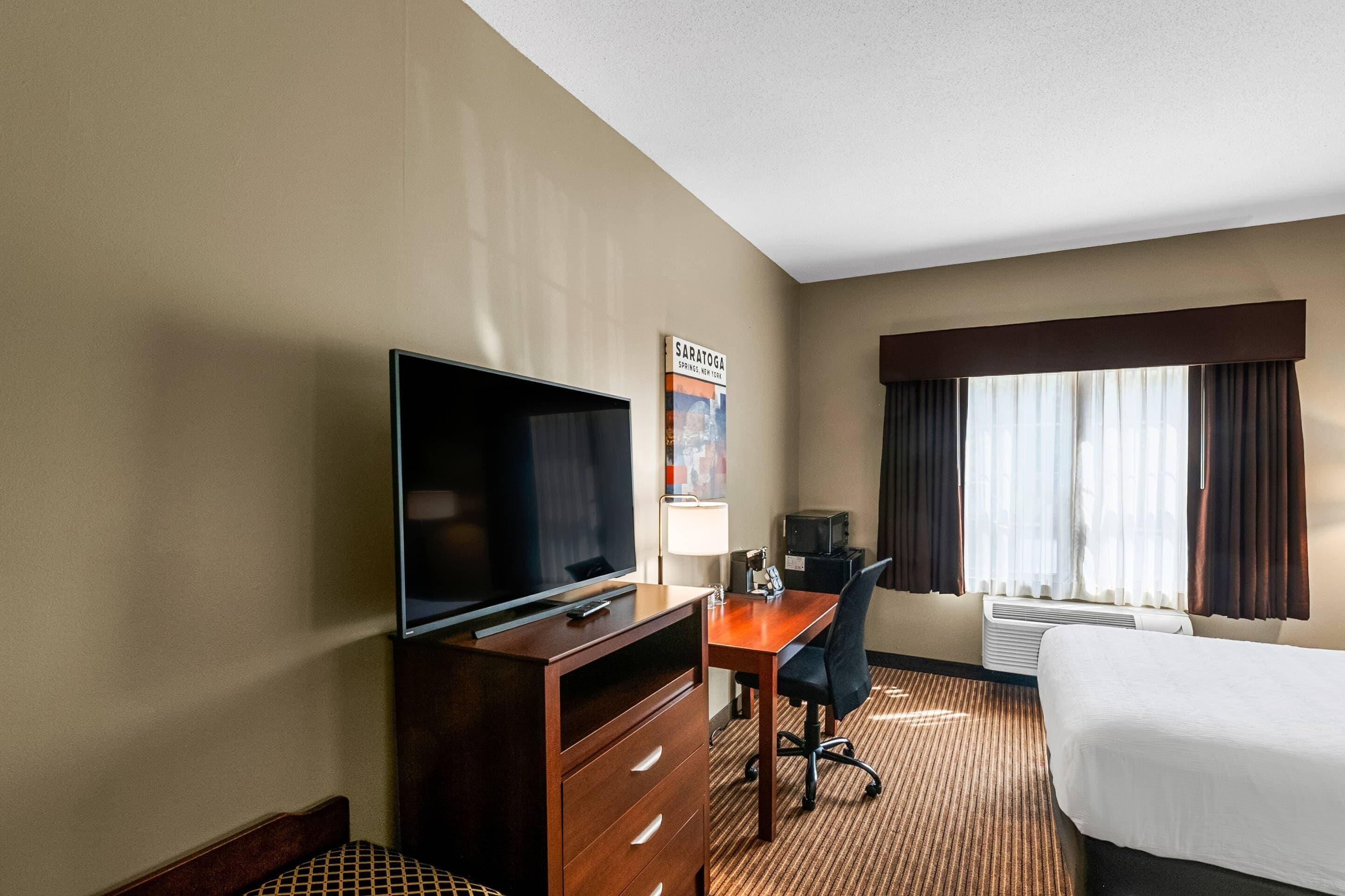 Une chambre d’hôtel avec un lit, un bureau et une chaise, une télévision et une affiche au mur.