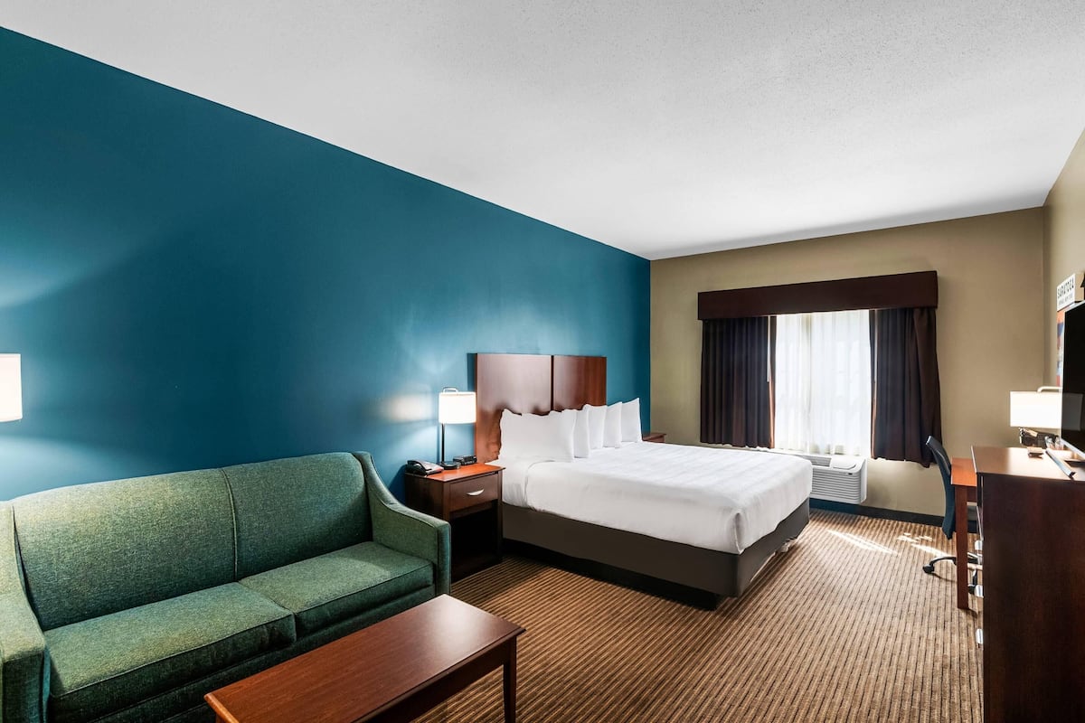 A hotel room with a bed, a green sofa, a desk, and a TV.
