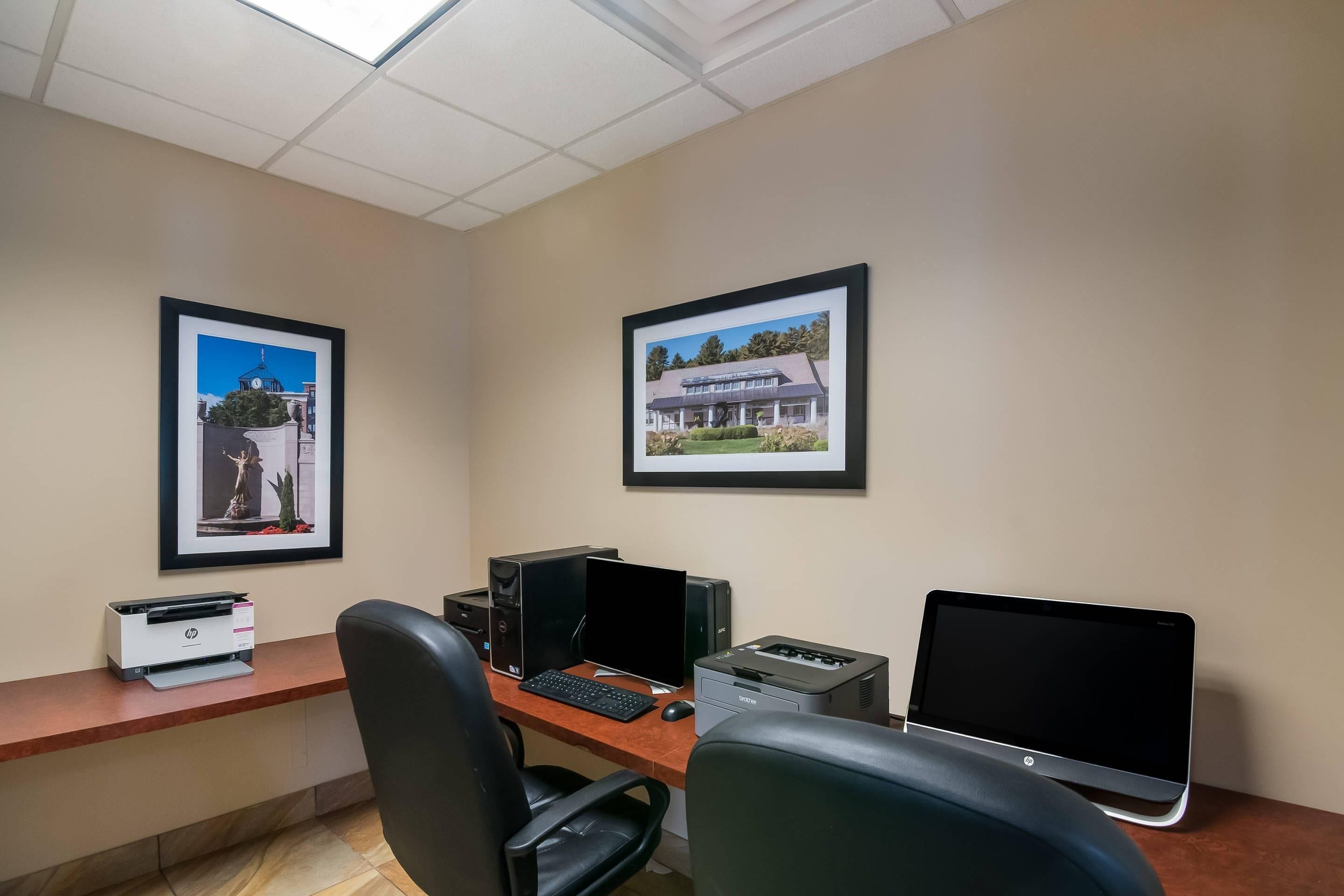 An office with two desks, computers, and framed pictures on the wall.
