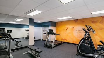 Ein Fitnessraum mit Laufbändern, Crosstrainern und einer Bank.