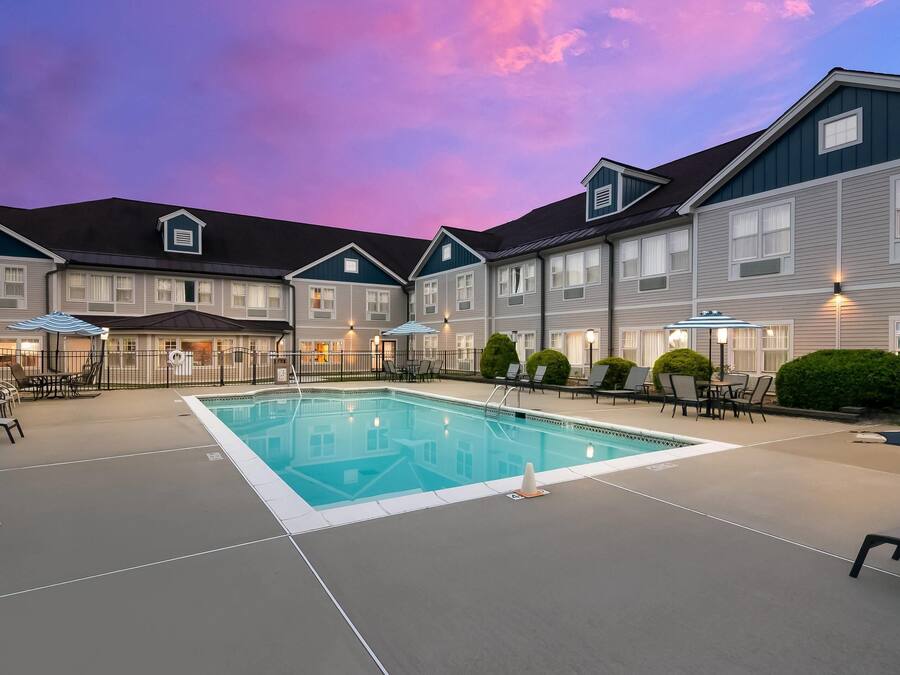 A hotel with a swimming pool, outdoor seating, and a sunset sky.