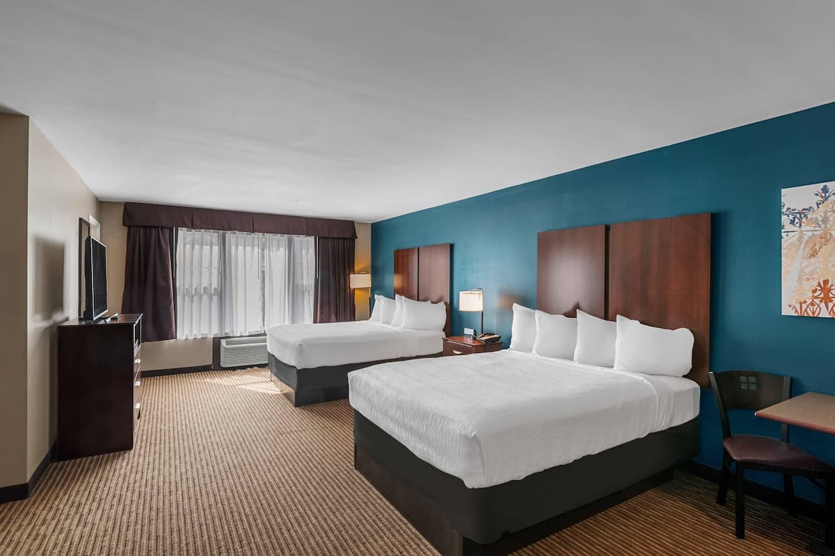 A hotel room with two beds, a desk, a chair, a TV, and a window with curtains.