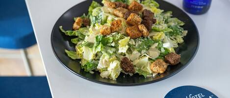 A plate of salad with croutons and cheese on a table with a blue coaster labeled "The Hotel Saratoga."