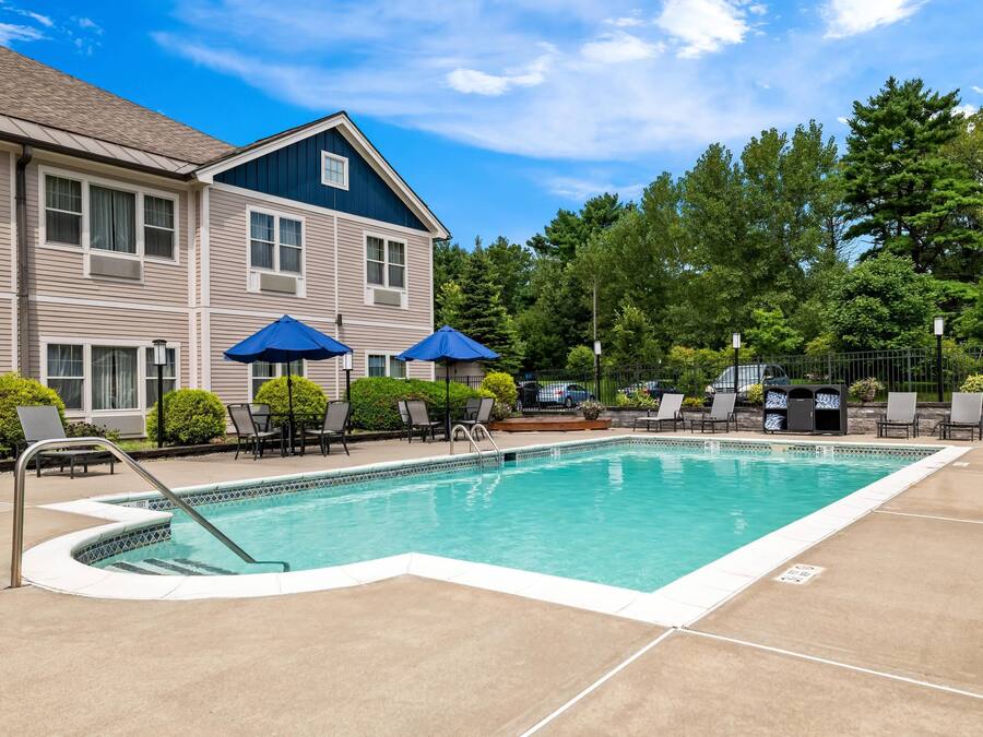 A swimming pool with lounge chairs and umbrellas, surrounded by a building with a blue roof and beige siding.
