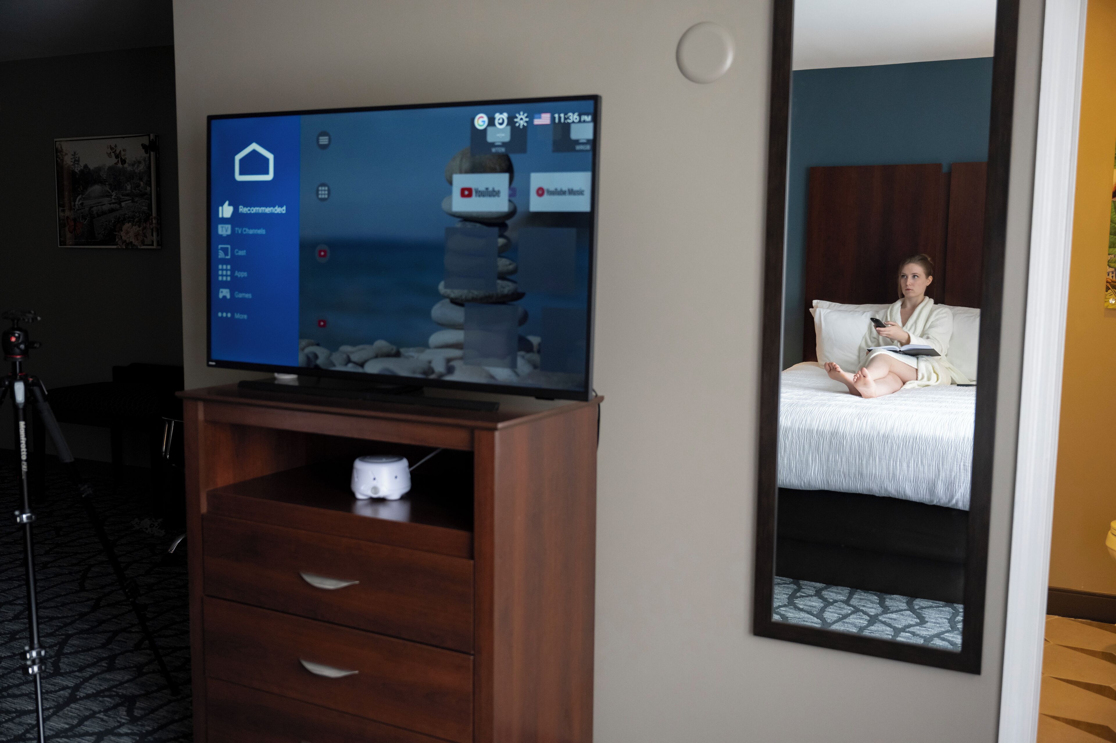 Ein Hotelzimmer mit Fernseher auf einem Holzboden, einem Bett mit weißer Bettdecke und einem Spiegel an der Wand.