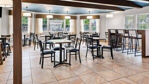 A spacious dining area with multiple tables and chairs, large windows with curtains, and a high ceiling with exposed beams. - The Hotel Saratoga, an Ascend Collection Hotel (Saratoga Springs)