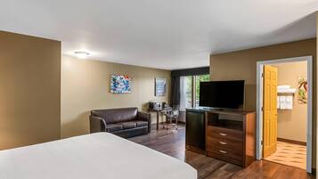 Una habitación de hotel con una cama, un escritorio, un televisor, un sofá y una puerta que da a un baño.