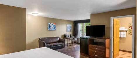 Una habitación de hotel con una cama, un escritorio, un televisor, un sofá y una puerta que da a un baño.