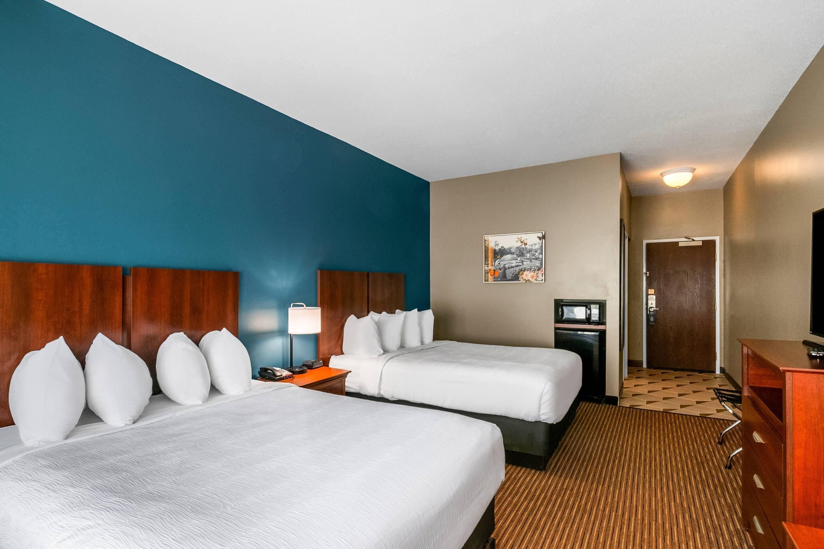 Een hotelkamer met twee bedden, een bureau, een televisie en een deur naar een andere kamer.