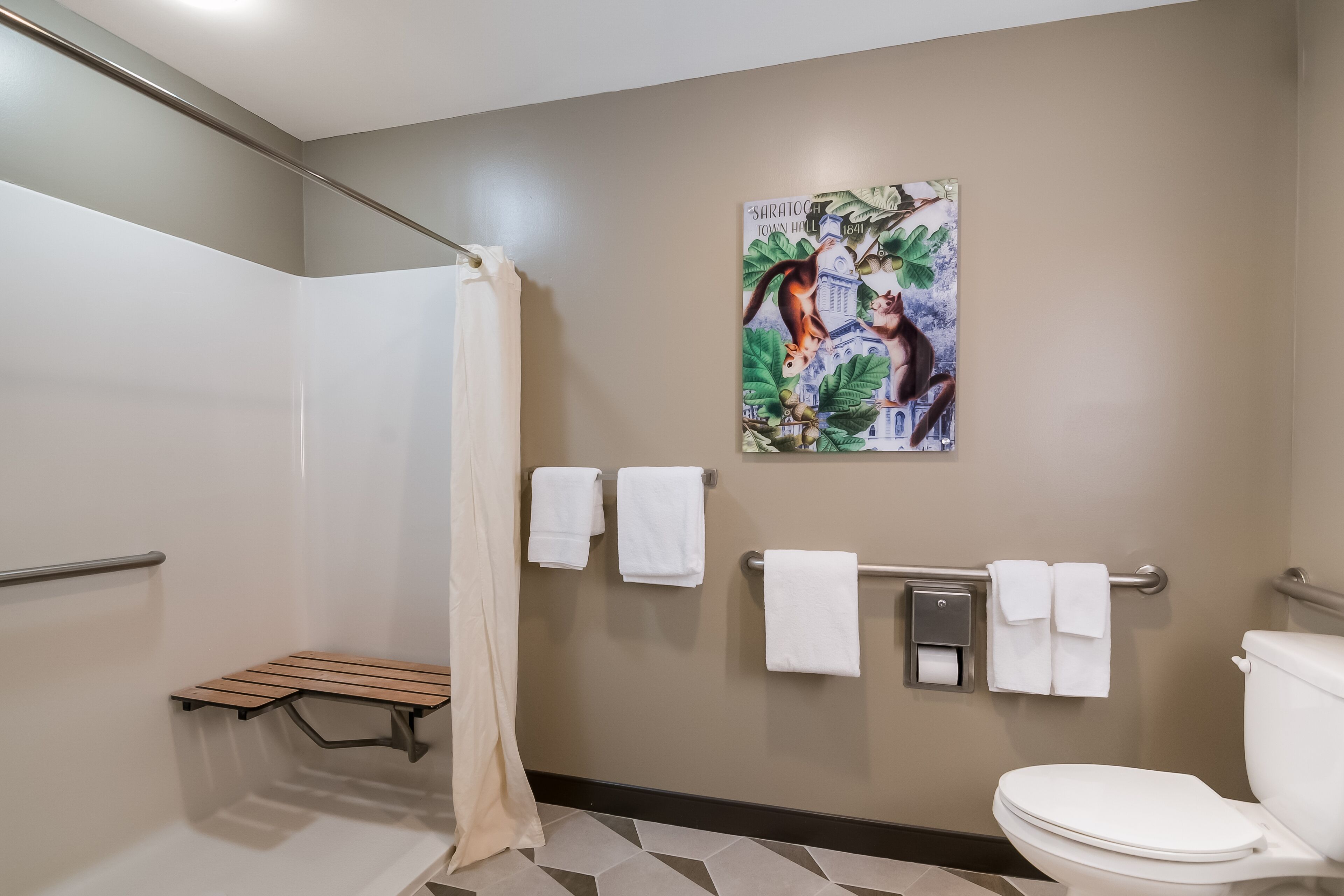 A bathroom with a shower, toilet, and a bench. There are towels hanging on a rack and a poster on the wall.