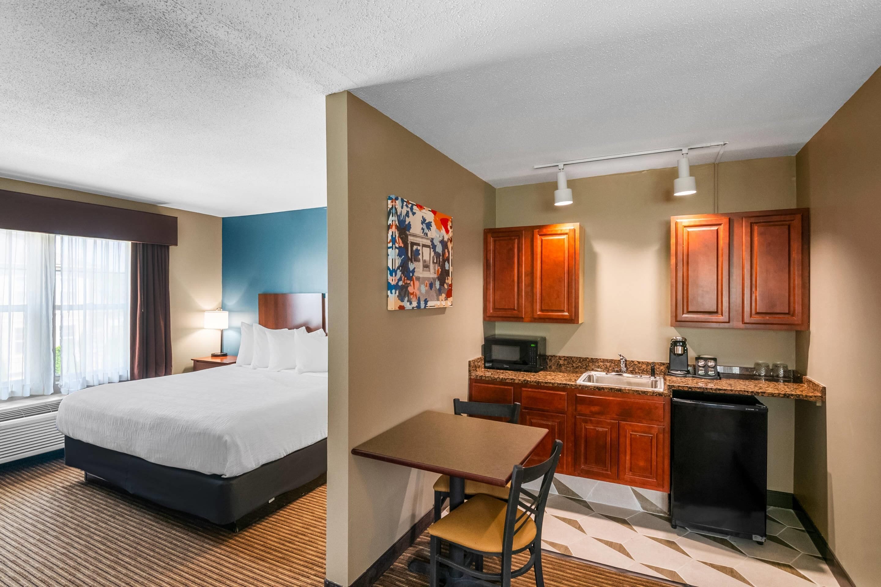 A hotel room with a bed, a desk, a chair, a microwave, a refrigerator, and a sink.