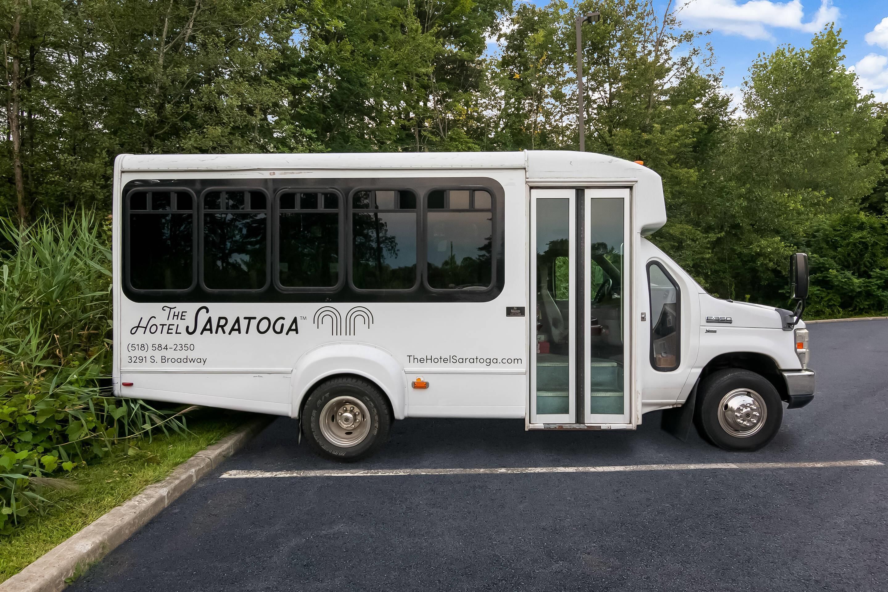 Un autobús blanco con la marca 'The Saratoga' estacionado al costado de una carretera.