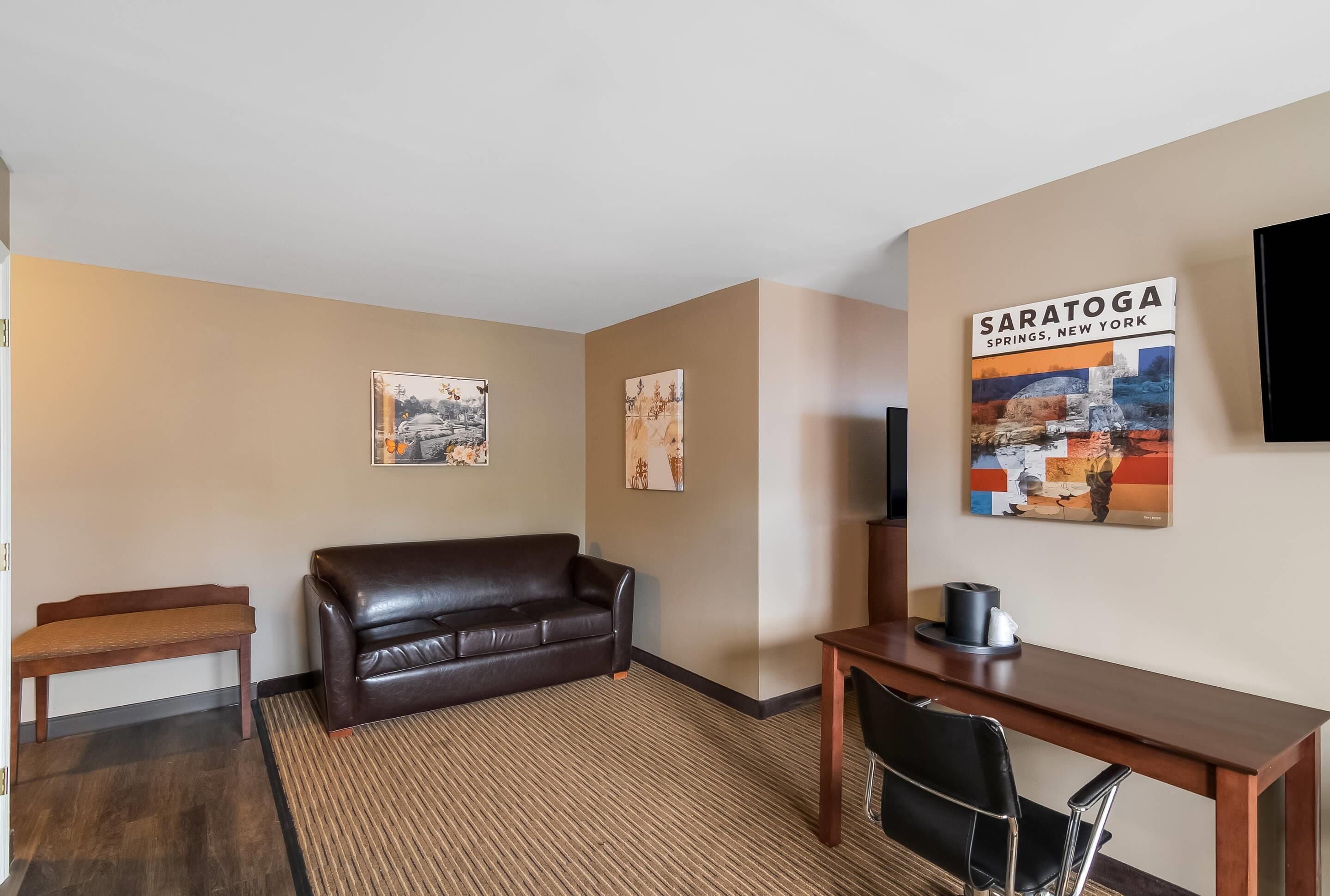 Habitación de hotel con un sofá de cuero marrón, un escritorio de madera y dos cuadros en las paredes.