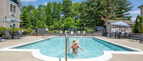 Une piscine où une femme nage, entourée de chaises longues et de parasols.
