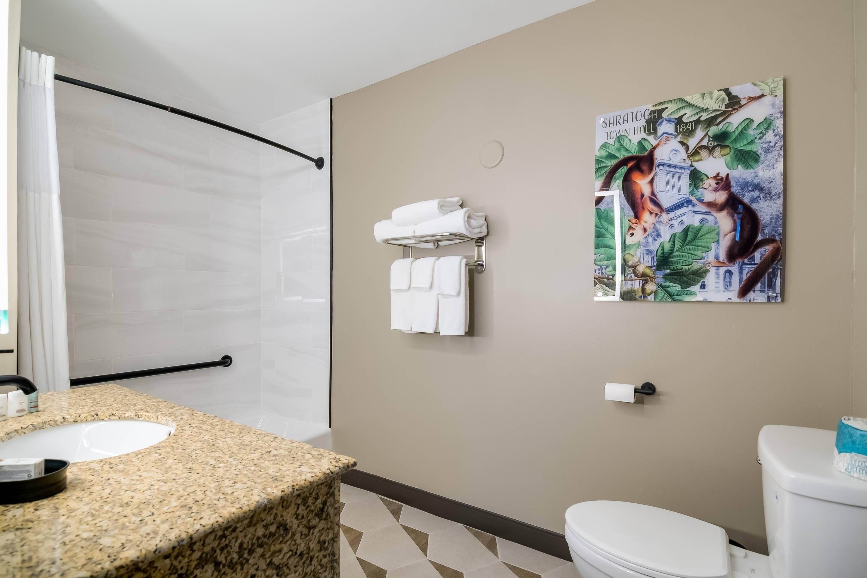 A bathroom with a granite countertop sink, a white toilet, a towel rack with folded towels, and a painting of a cat on a tree branch.