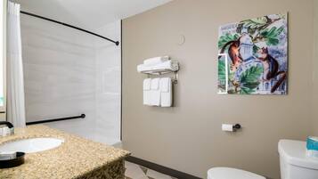 Un baño con lavamanos de encimera de granito, un inodoro blanco, un perchero con toallas dobladas y un cuadro de un gato en una rama de árbol.